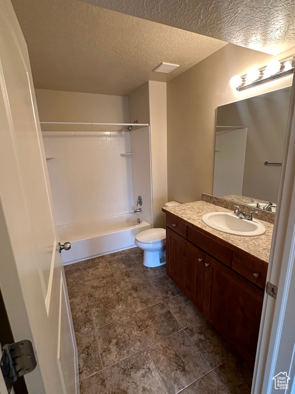 Bathroom with a textured ceiling, shower / bathing tub combination, vanity, and toilet