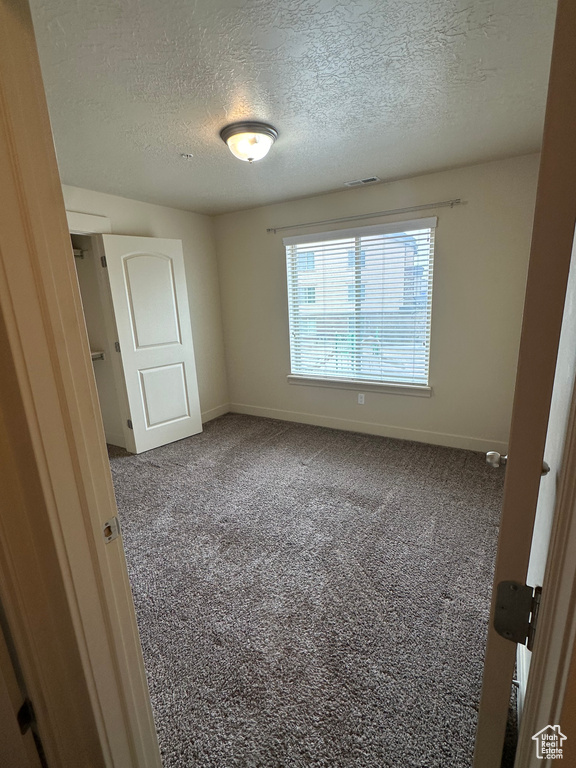 Unfurnished bedroom featuring a textured ceiling, carpet floors, and baseboards