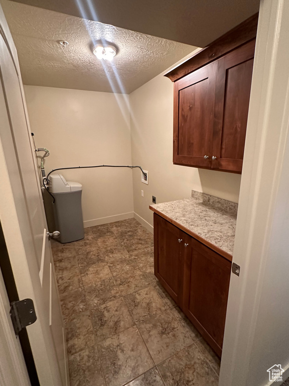Washroom with a textured ceiling, hookup for an electric dryer, washer hookup, baseboards, and cabinet space