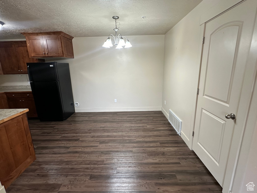 Kitchen with dark wood-type flooring, visible vents, light countertops, freestanding refrigerator, and an inviting chandelier