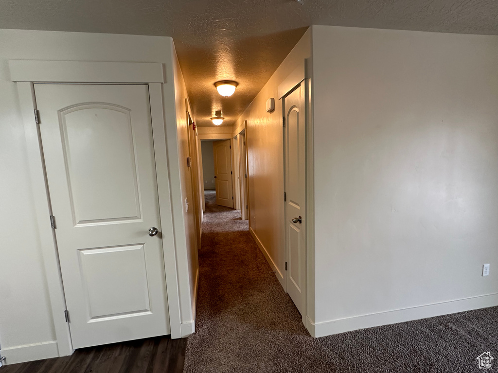 Corridor with dark colored carpet, a textured ceiling, and baseboards