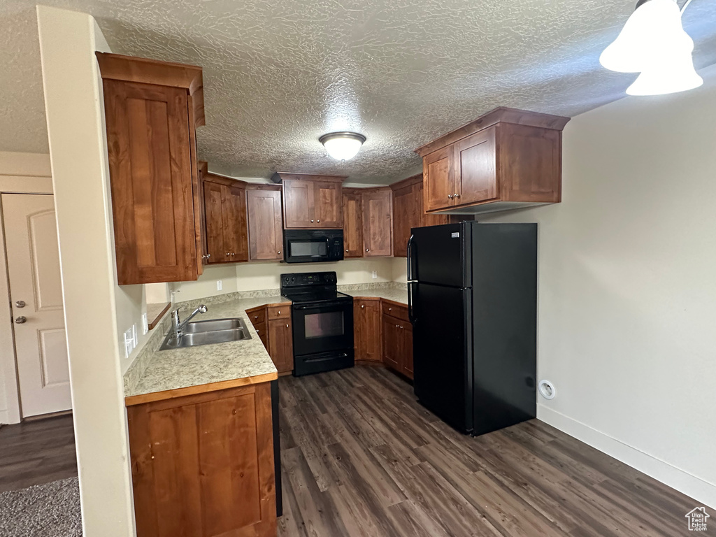 Kitchen with a textured ceiling, dark wood-style flooring, a sink, light countertops, and black appliances