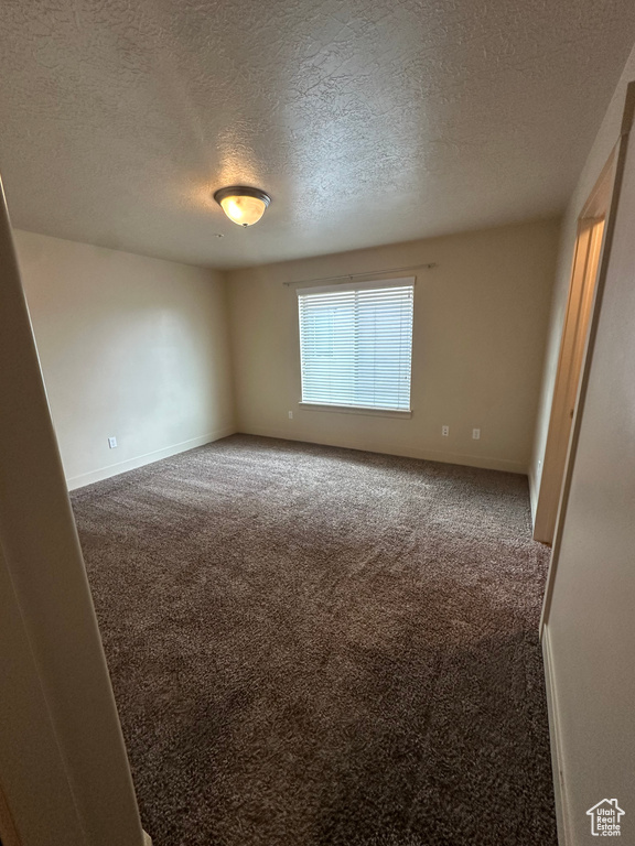 Spare room featuring carpet flooring, a textured ceiling, and baseboards