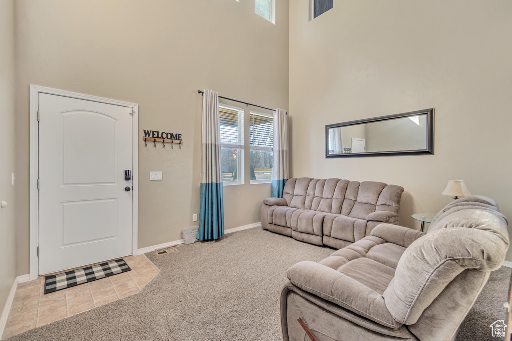 Carpeted living room with visible vents, a towering ceiling, baseboards, and tile patterned floors