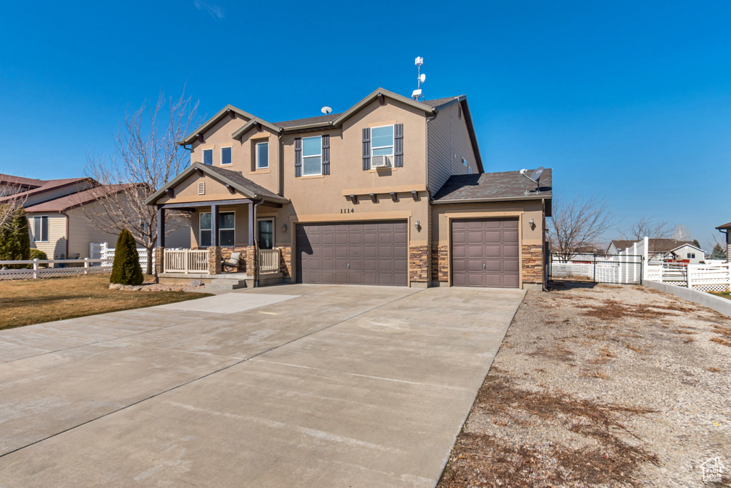 View of front of property with a garage, driveway, covered porch, fence, and stucco siding