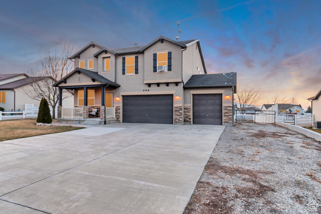 View of front of home with driveway, stone siding, fence, a porch, and stucco siding