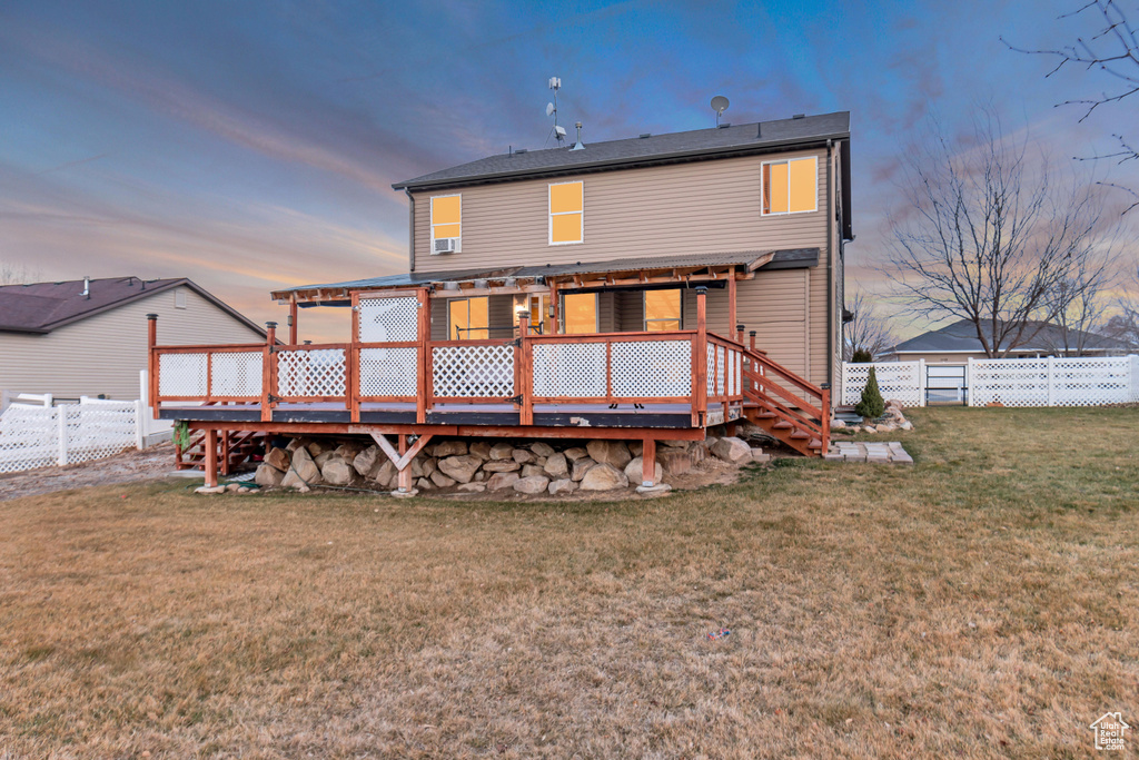 Back of house at dusk with a lawn, a fenced backyard, a wooden deck, and a pergola