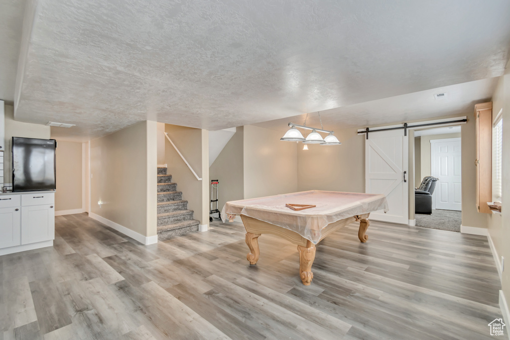 Recreation room with pool table, a barn door, light wood-style floors, a textured ceiling, and baseboards