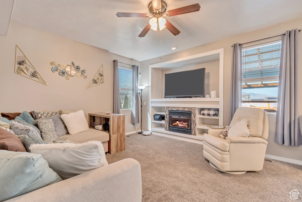 Living room featuring built in shelves, a glass covered fireplace, carpet flooring, ceiling fan, and baseboards