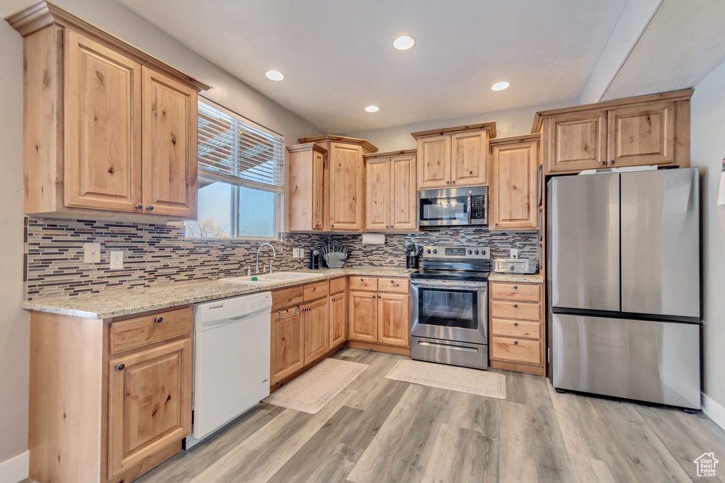 Kitchen featuring stainless steel appliances, backsplash, light wood-style floors, light brown cabinets, and a sink