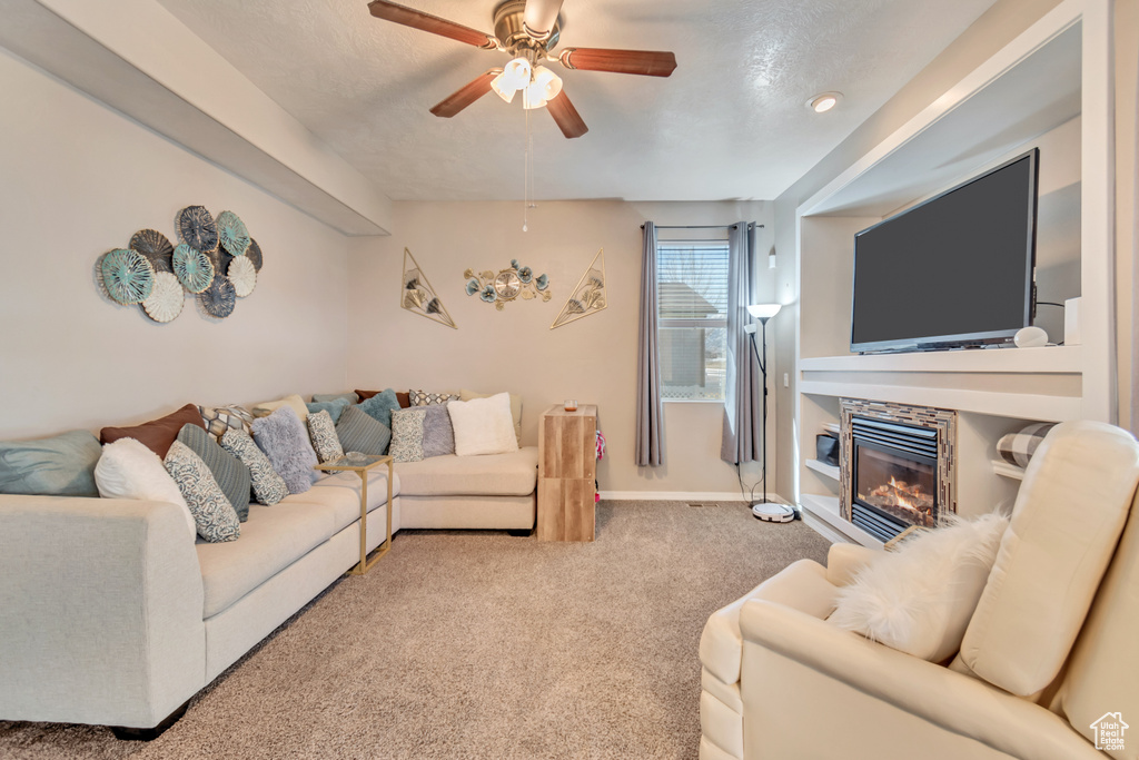 Carpeted living area with baseboards, a ceiling fan, and a stone fireplace