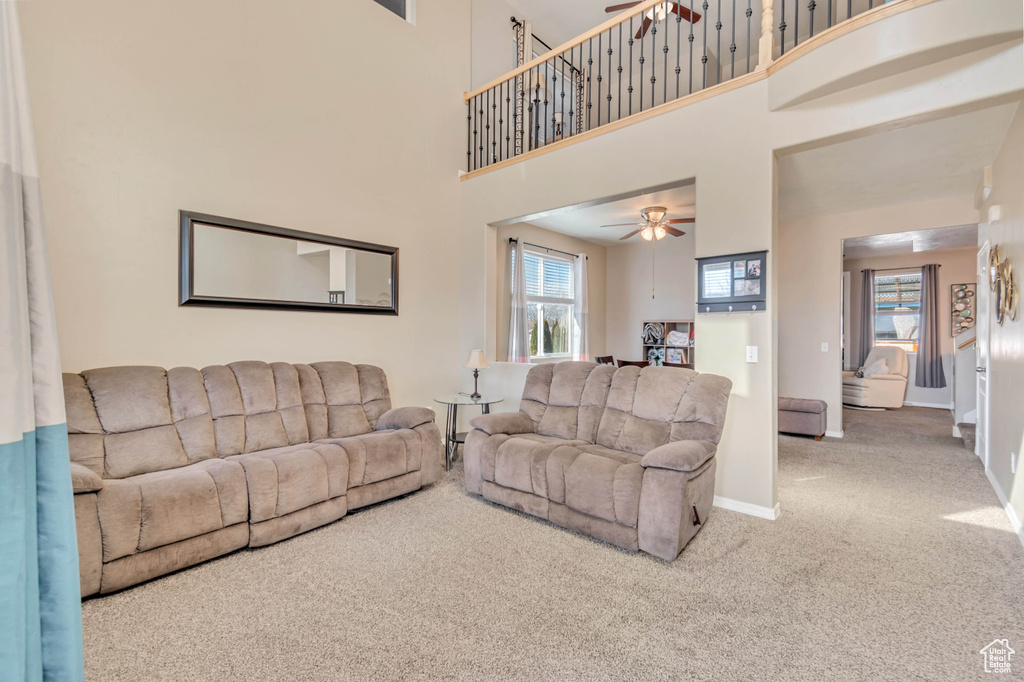 Carpeted living area with a towering ceiling, plenty of natural light, baseboards, and ceiling fan