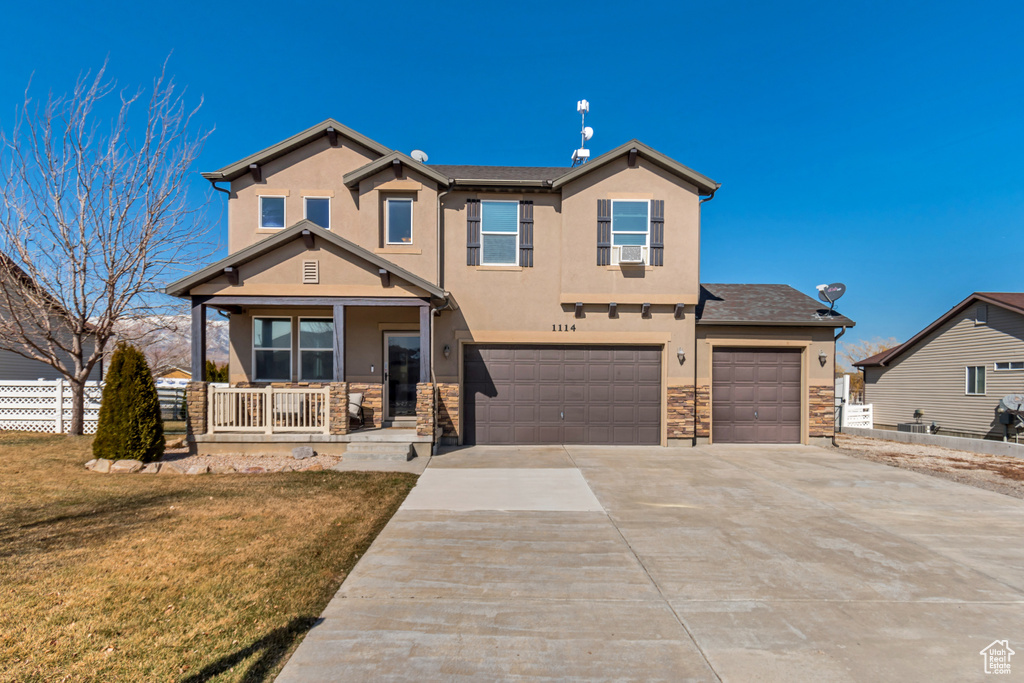 View of front facade featuring stone siding, stucco siding, covered porch, fence, and a front yard