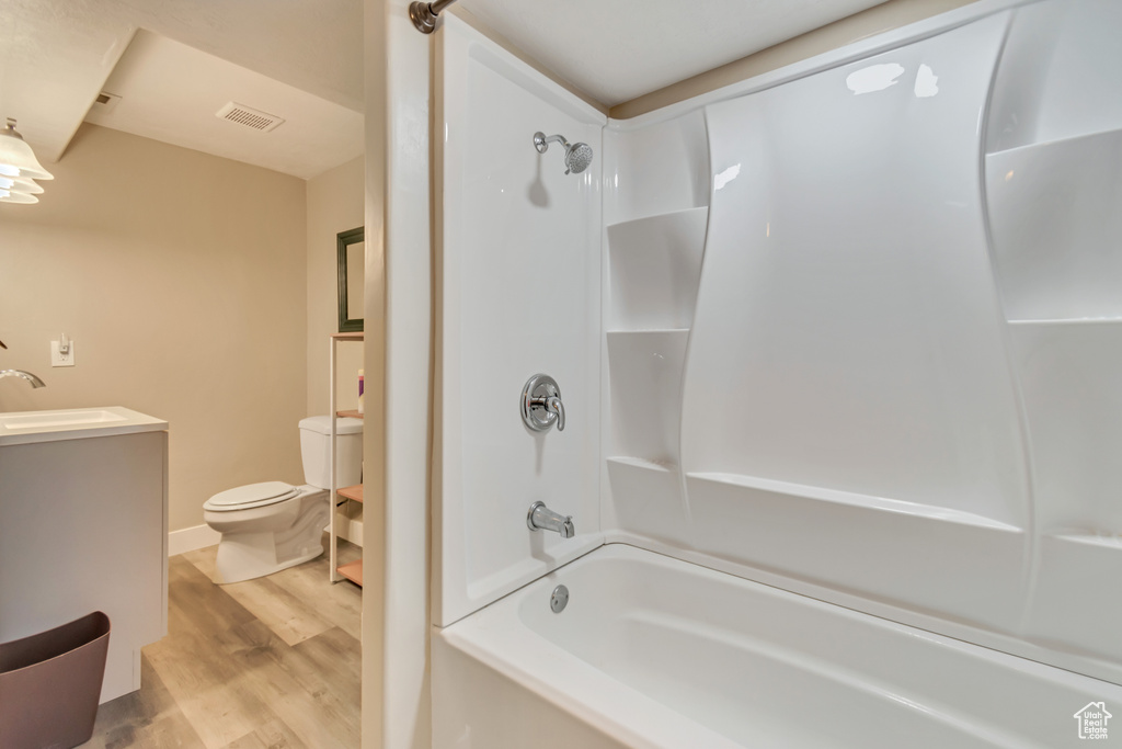 Full bath featuring bathing tub / shower combination, visible vents, toilet, vanity, and wood finished floors