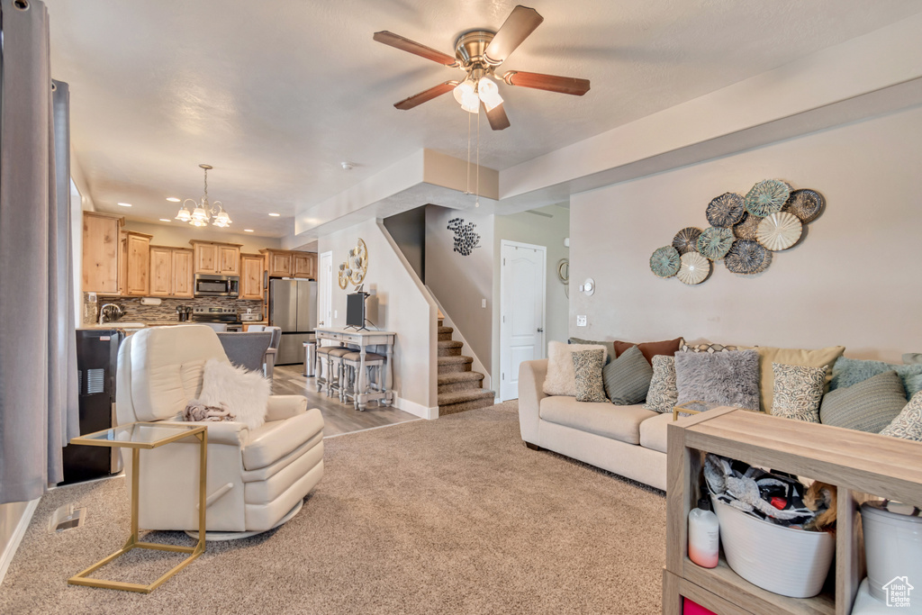 Living room featuring recessed lighting, ceiling fan with notable chandelier, light colored carpet, baseboards, and stairs