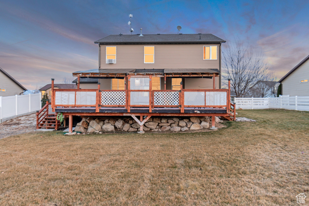 Back of house at dusk featuring a fenced backyard, a lawn, and a deck