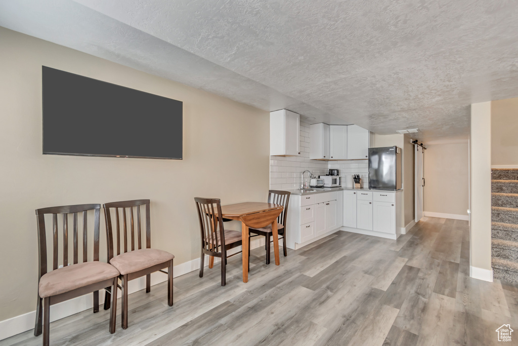 Kitchen with white cabinets, light wood-style flooring, decorative backsplash, and a sink