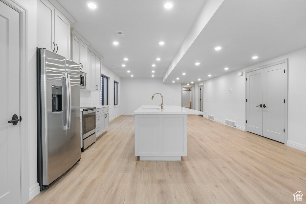 Kitchen featuring visible vents, white cabinets, an island with sink, appliances with stainless steel finishes, and light wood-type flooring