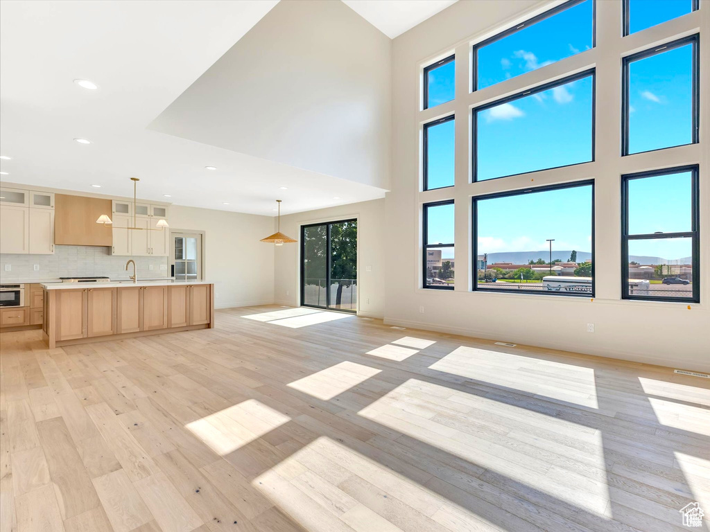 Unfurnished living room with a high ceiling, recessed lighting, a sink, and light wood-style floors