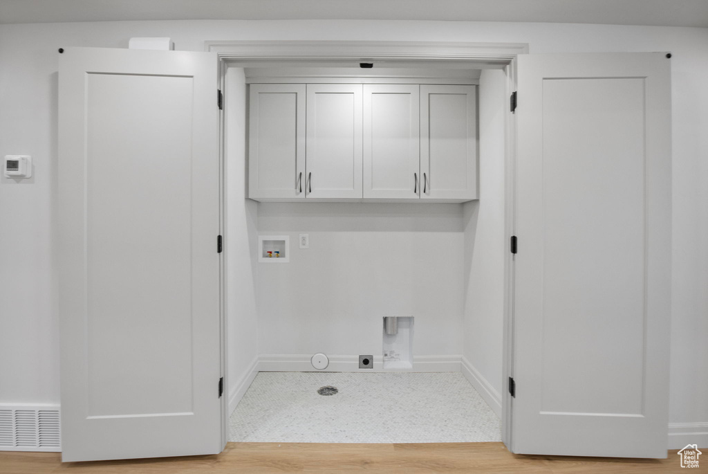 Laundry area with hookup for a washing machine, light wood-style flooring, hookup for an electric dryer, hookup for a gas dryer, and cabinet space