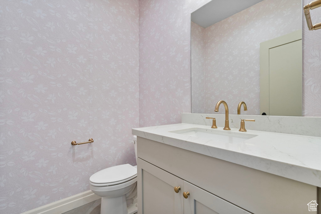 Bathroom featuring baseboards, vanity, toilet, and wallpapered walls