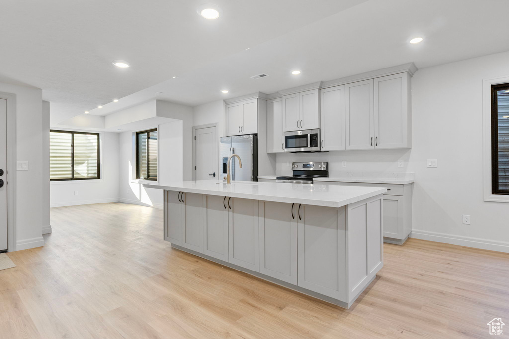 Kitchen featuring light countertops, appliances with stainless steel finishes, a center island with sink, and recessed lighting