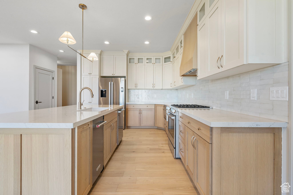 Kitchen with tasteful backsplash, a center island with sink, appliances with stainless steel finishes, light wood-type flooring, and a sink