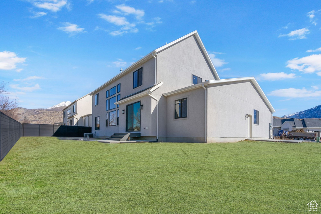 Back of house with a mountain view, a yard, fence, and stucco siding