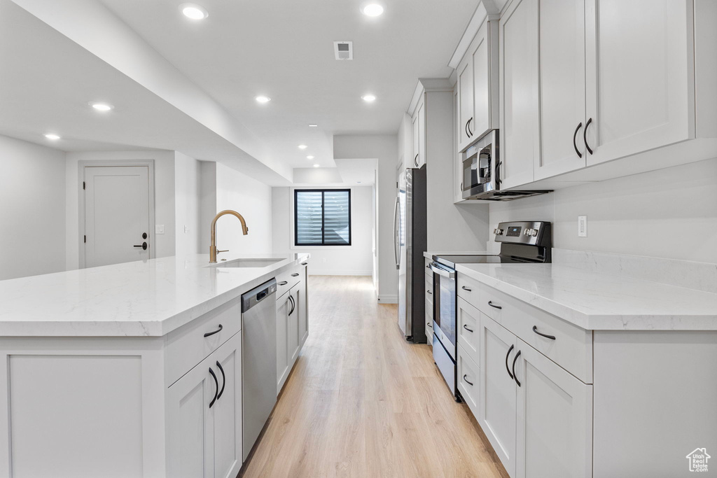 Kitchen featuring light wood finished floors, stainless steel appliances, white cabinetry, a sink, and an island with sink