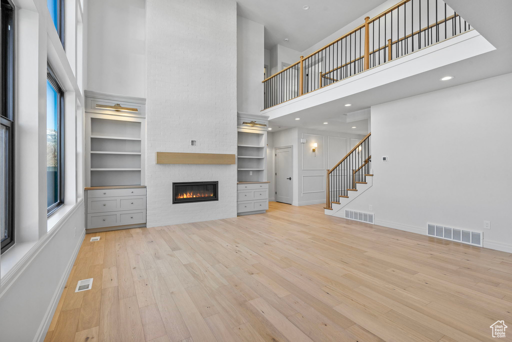 Unfurnished living room featuring stairway, wood-type flooring, a towering ceiling, and visible vents