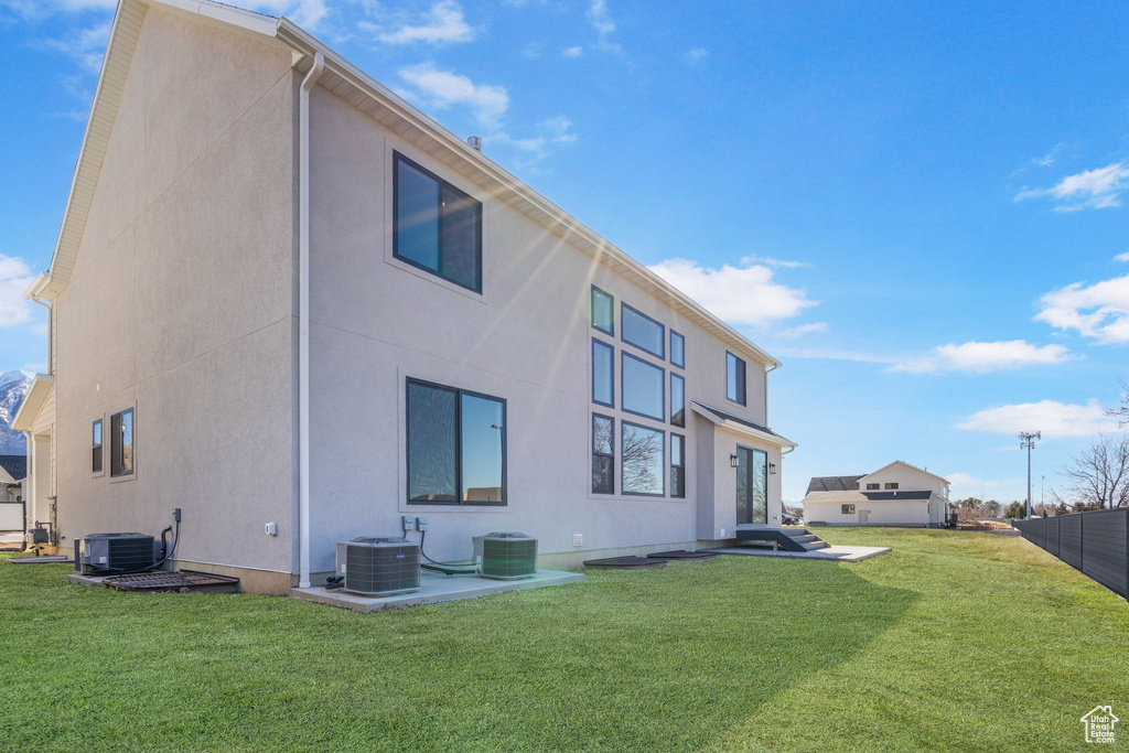 Rear view of property with a yard, fence, cooling unit, and stucco siding