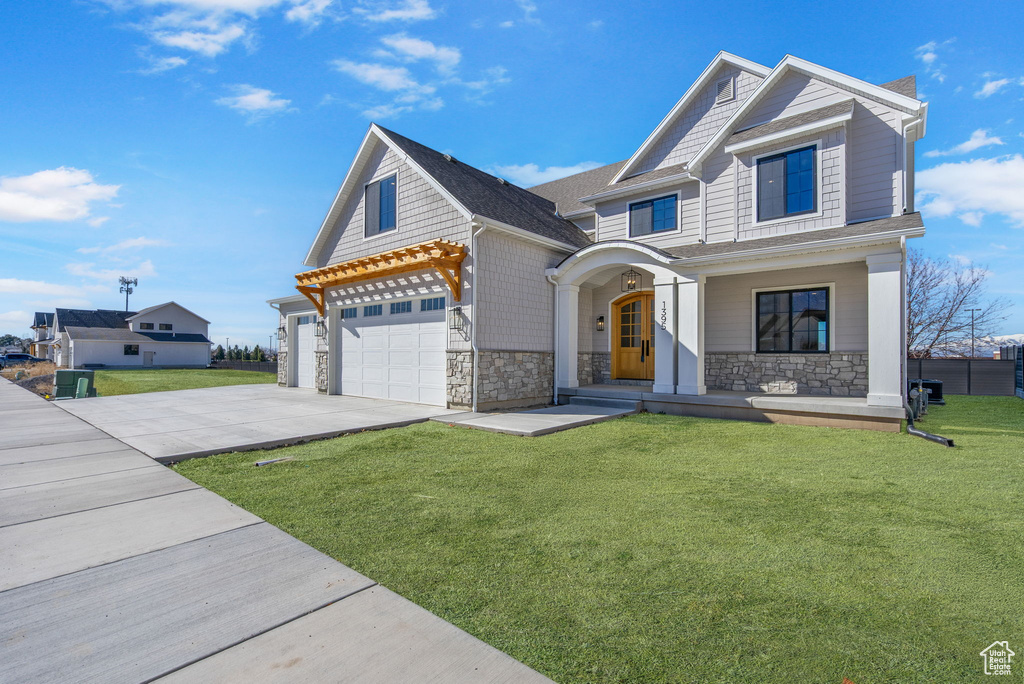 View of front of house with an attached garage, concrete driveway, a front lawn, and stone siding