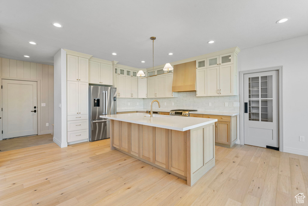 Kitchen featuring premium range hood, light countertops, light wood-type flooring, range, and stainless steel fridge with ice dispenser