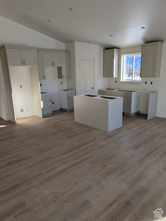 Kitchen featuring lofted ceiling, a center island, gray cabinetry, and wood finished floors