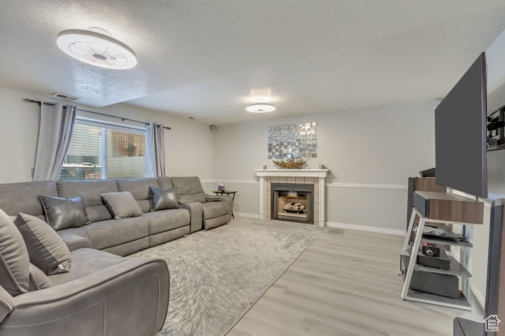 Living area with a textured ceiling, a tile fireplace, visible vents, baseboards, and light wood finished floors