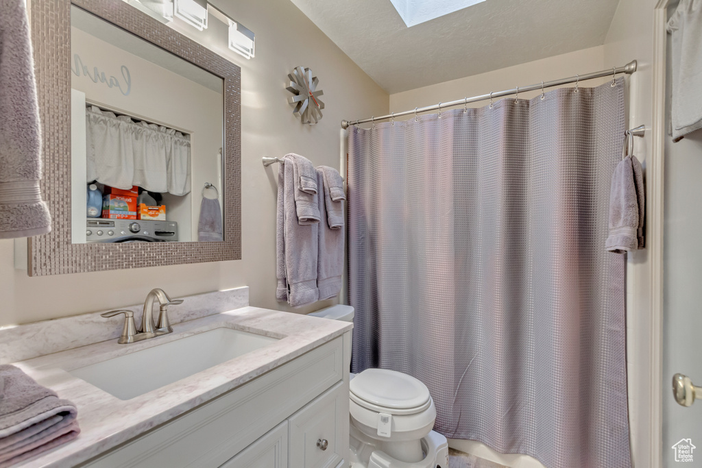 Bathroom with a skylight, a shower with shower curtain, vanity, and toilet