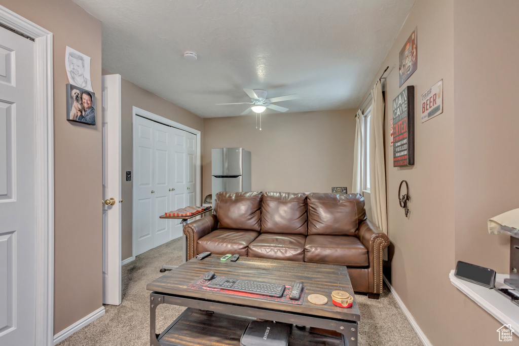 Living area featuring light colored carpet, ceiling fan, and baseboards