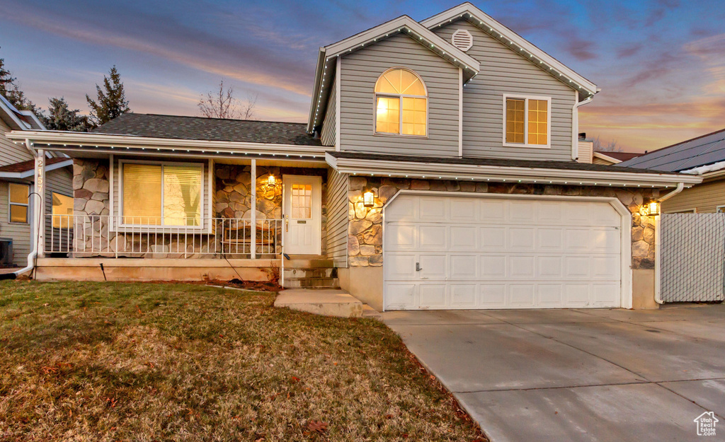 Traditional-style home with covered porch, concrete driveway, an attached garage, stone siding, and a front lawn