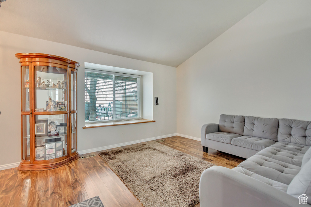 Living area featuring baseboards, visible vents, vaulted ceiling, and wood finished floors