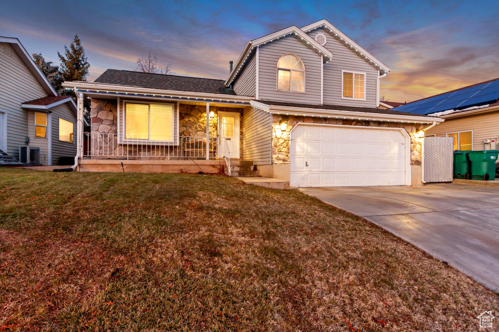 Traditional-style home with a porch, central AC unit, stone siding, driveway, and a front lawn