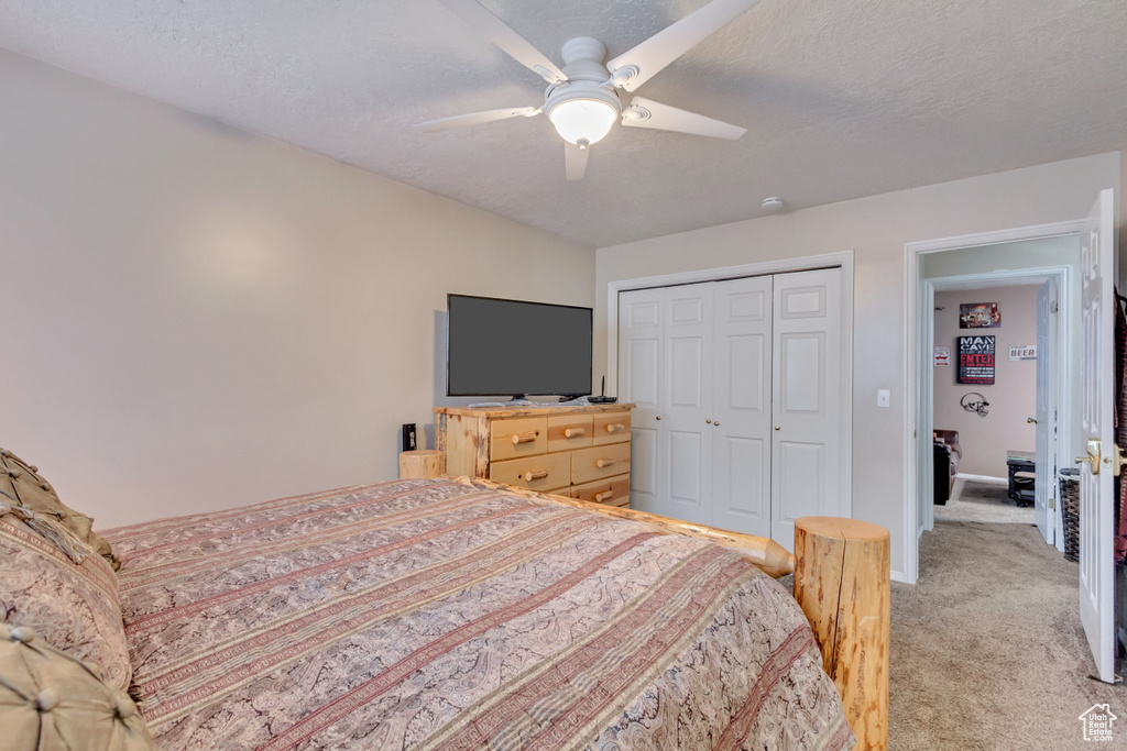 Bedroom with light carpet, ceiling fan, a textured ceiling, and a closet