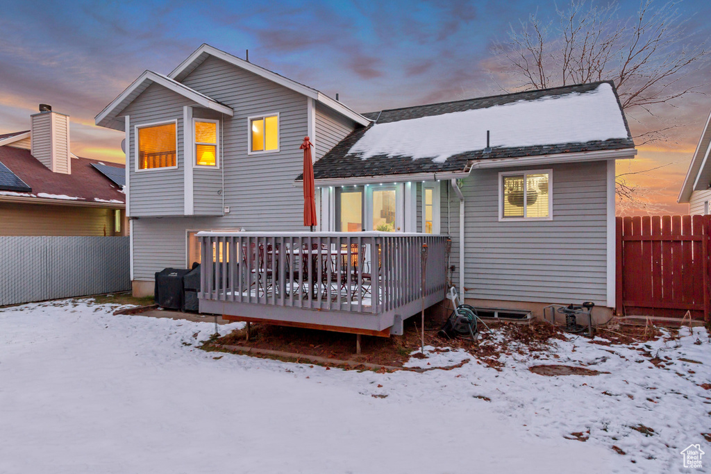 Snow covered rear of property with fence and a deck