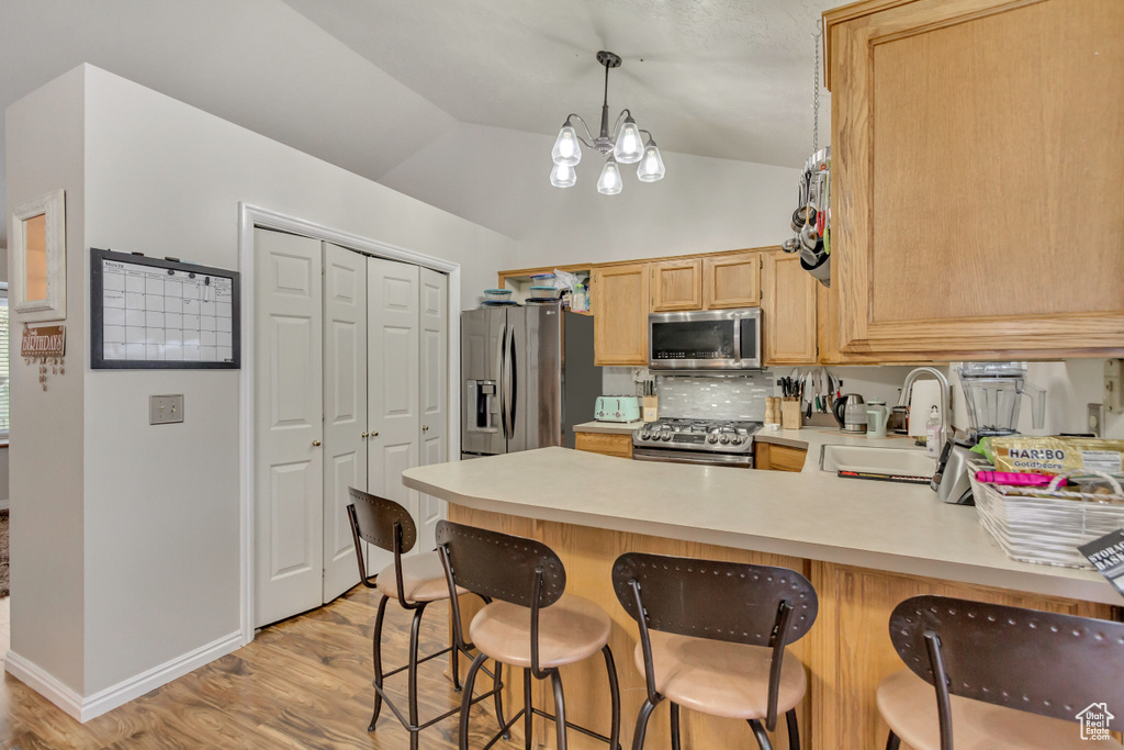 Kitchen featuring appliances with stainless steel finishes, a peninsula, light countertops, light wood-style floors, and a sink