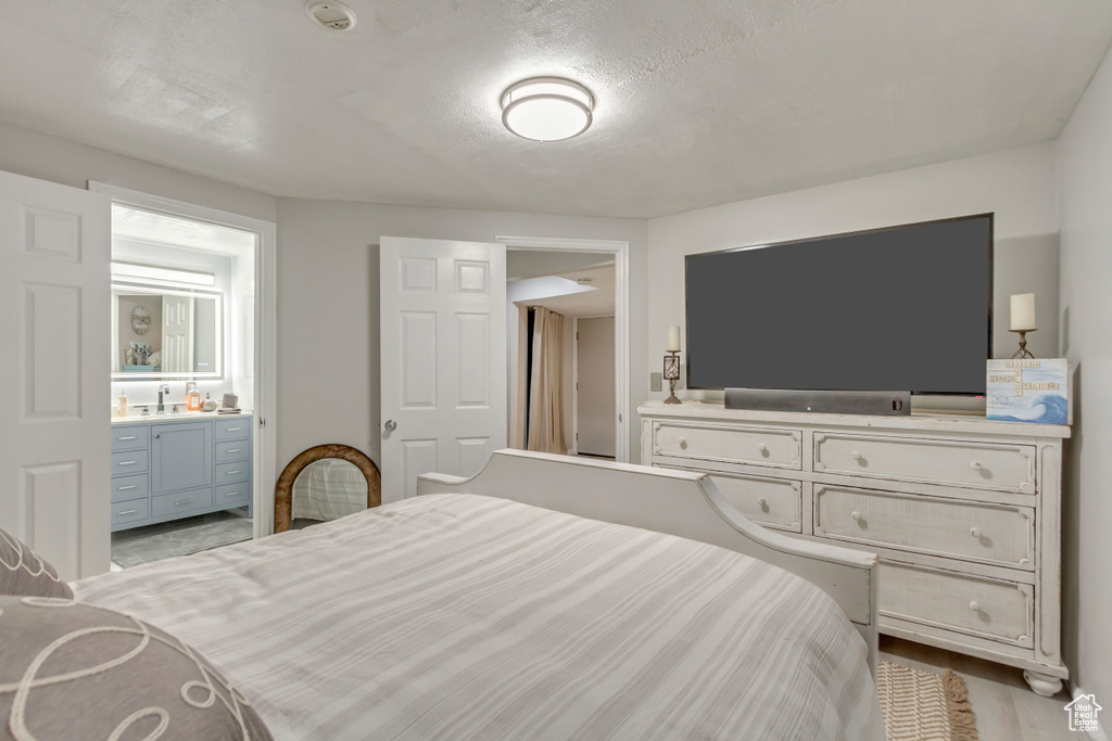 Bedroom with a sink, wood finished floors, a textured ceiling, and ensuite bath