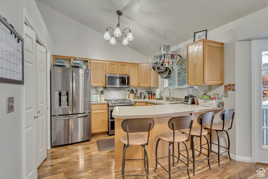 Kitchen with light brown cabinetry, appliances with stainless steel finishes, a sink, a chandelier, and a peninsula