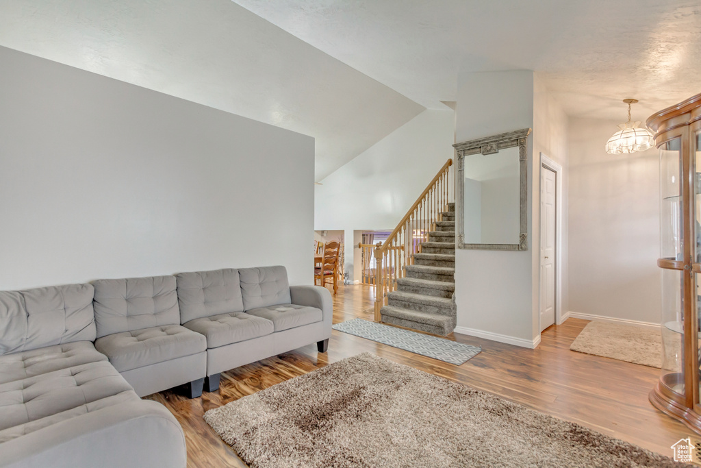 Living area with baseboards, wood finished floors, stairs, vaulted ceiling, and a chandelier