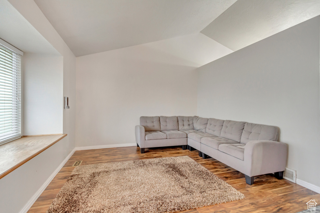 Living room with vaulted ceiling, visible vents, light wood-style flooring, and baseboards