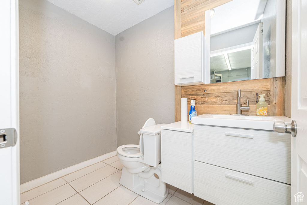 Half bath featuring toilet, vanity, baseboards, and tile patterned floors