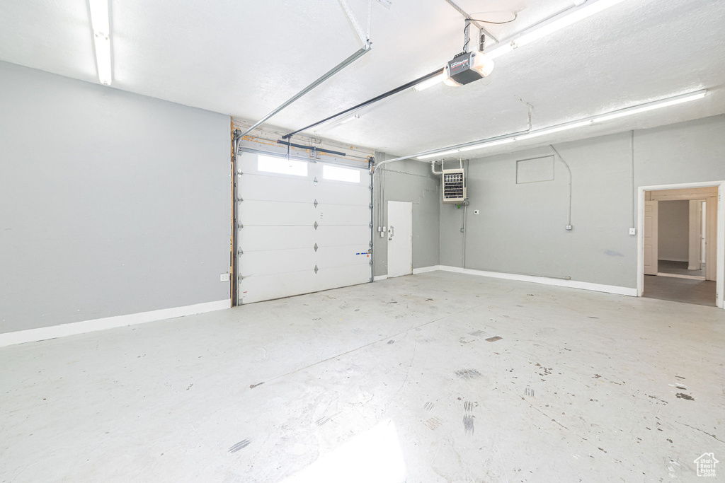 Garage with a wall mounted AC, baseboards, and a garage door opener