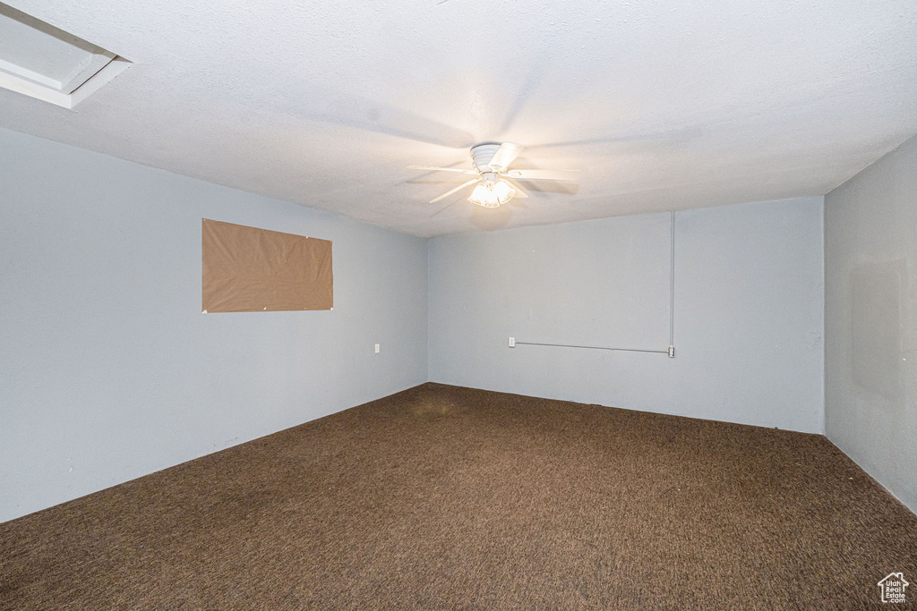 Empty room with a textured ceiling, dark colored carpet, and attic access